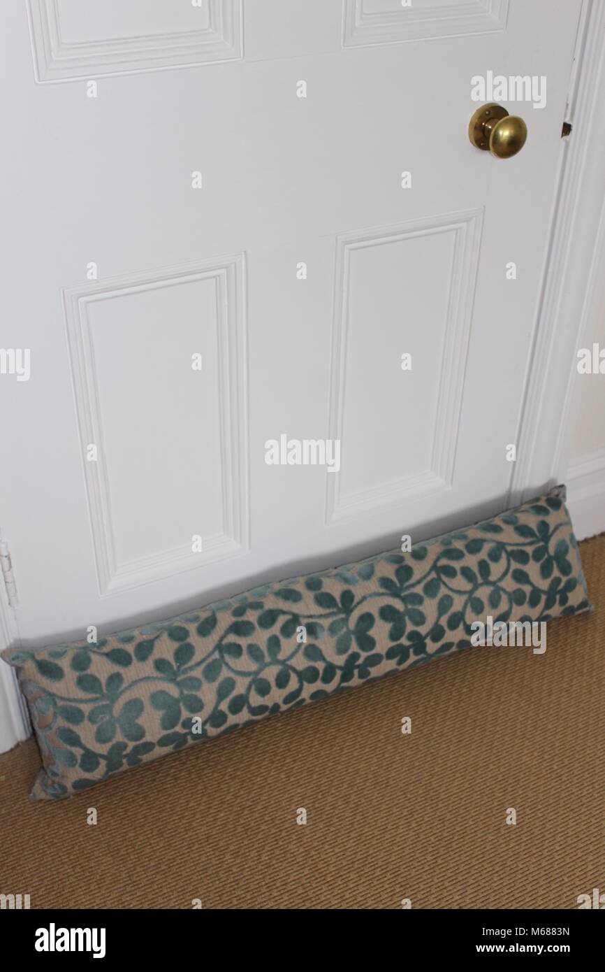 Turquoise and cream draught excluder against a white panelled door on a sand coloured carpet Stock Photo