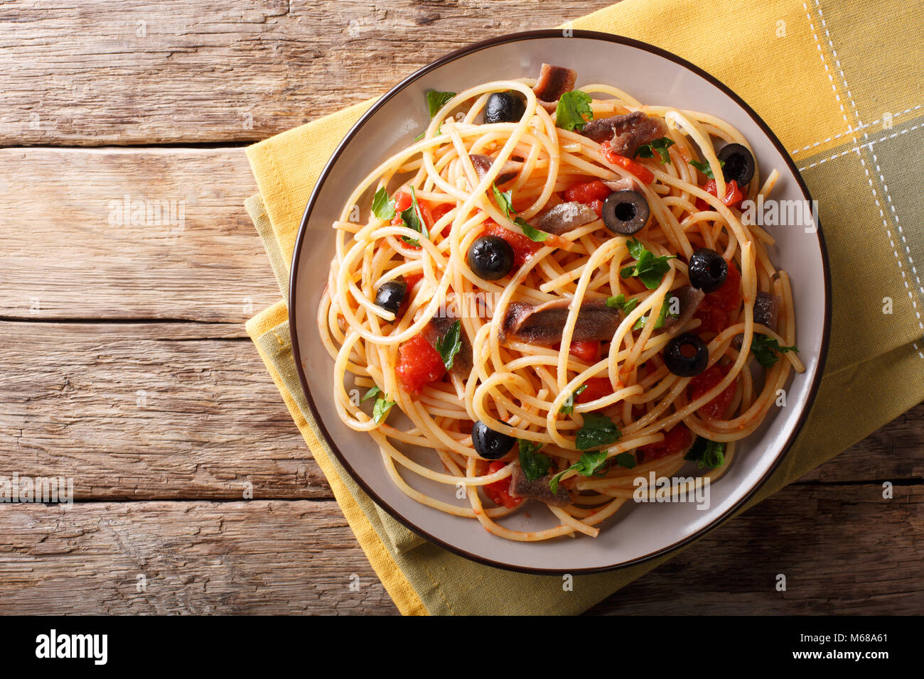 Traditional pasta alla puttanesca with anchovies, tomatoes, garlic and black olives close-up on a plate on the table. horizontal top view from above Stock Photo