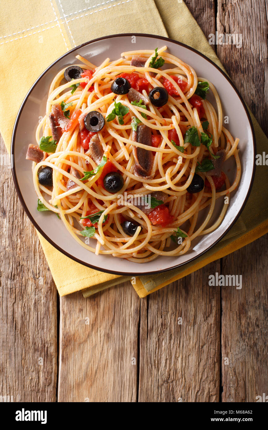 Spaghetti alla putanesca with anchovies, tomatoes, garlic and black olives close-up on a plate. Vertical top view from above Stock Photo