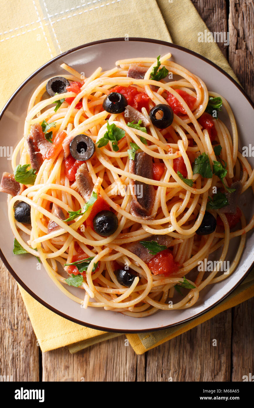 Pasta Alla Puttanesca with anchovies and black olives on a plate. Vertical top view from above Stock Photo
