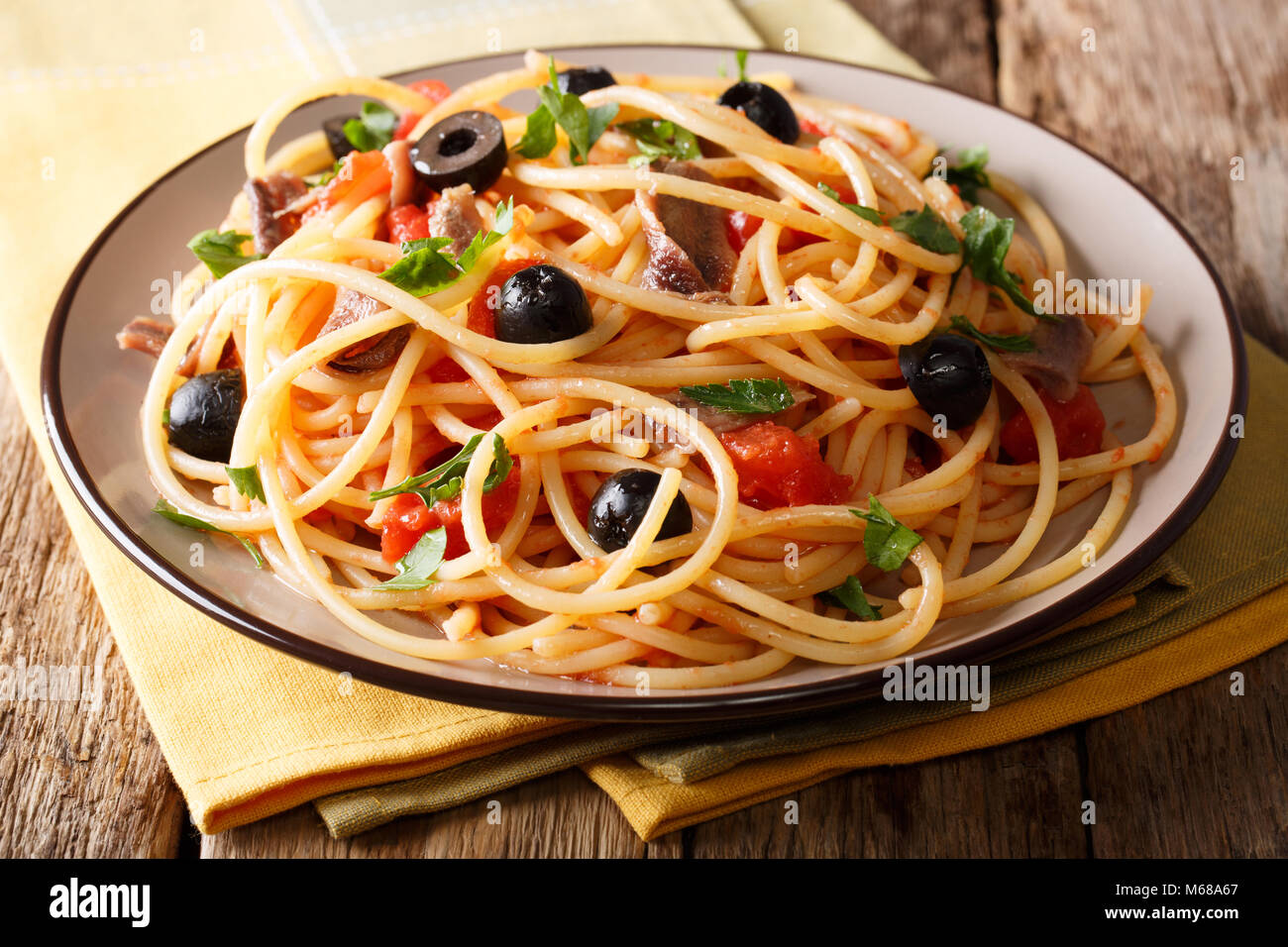 Delicious spaghetti alla putanesca with anchovies with vegetables and greens close-up on a plate. horizontal Stock Photo
