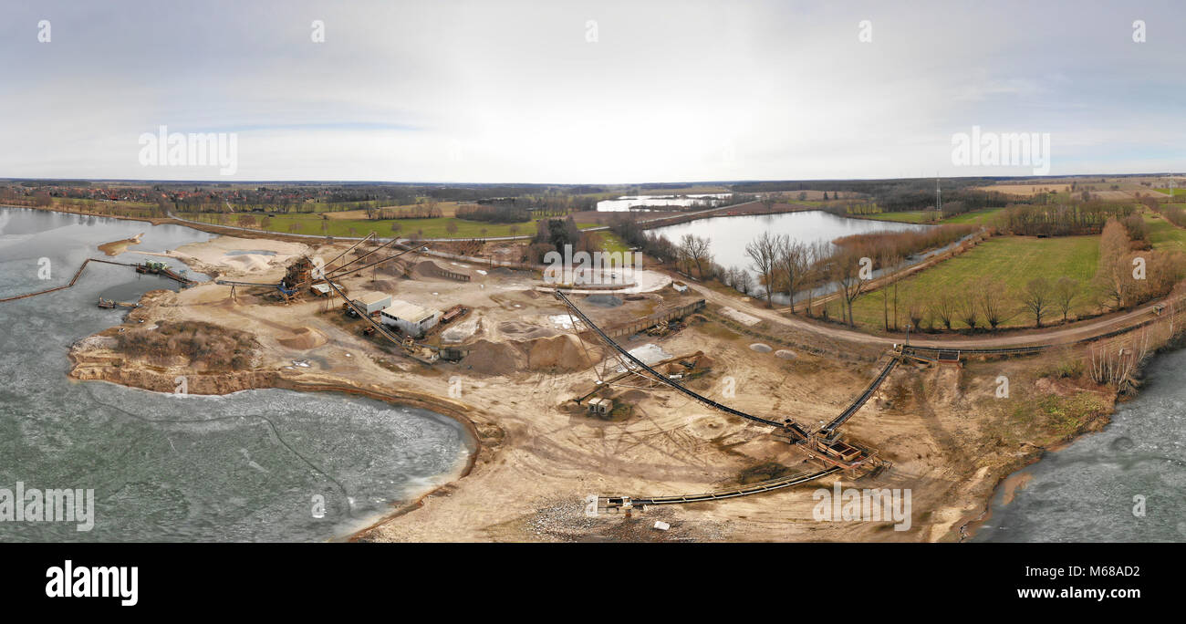 Composite panorama of aerial photographs and aerial photos of a wet quarry for gravel and sand with an almost frozen lake and large machines for excav Stock Photo