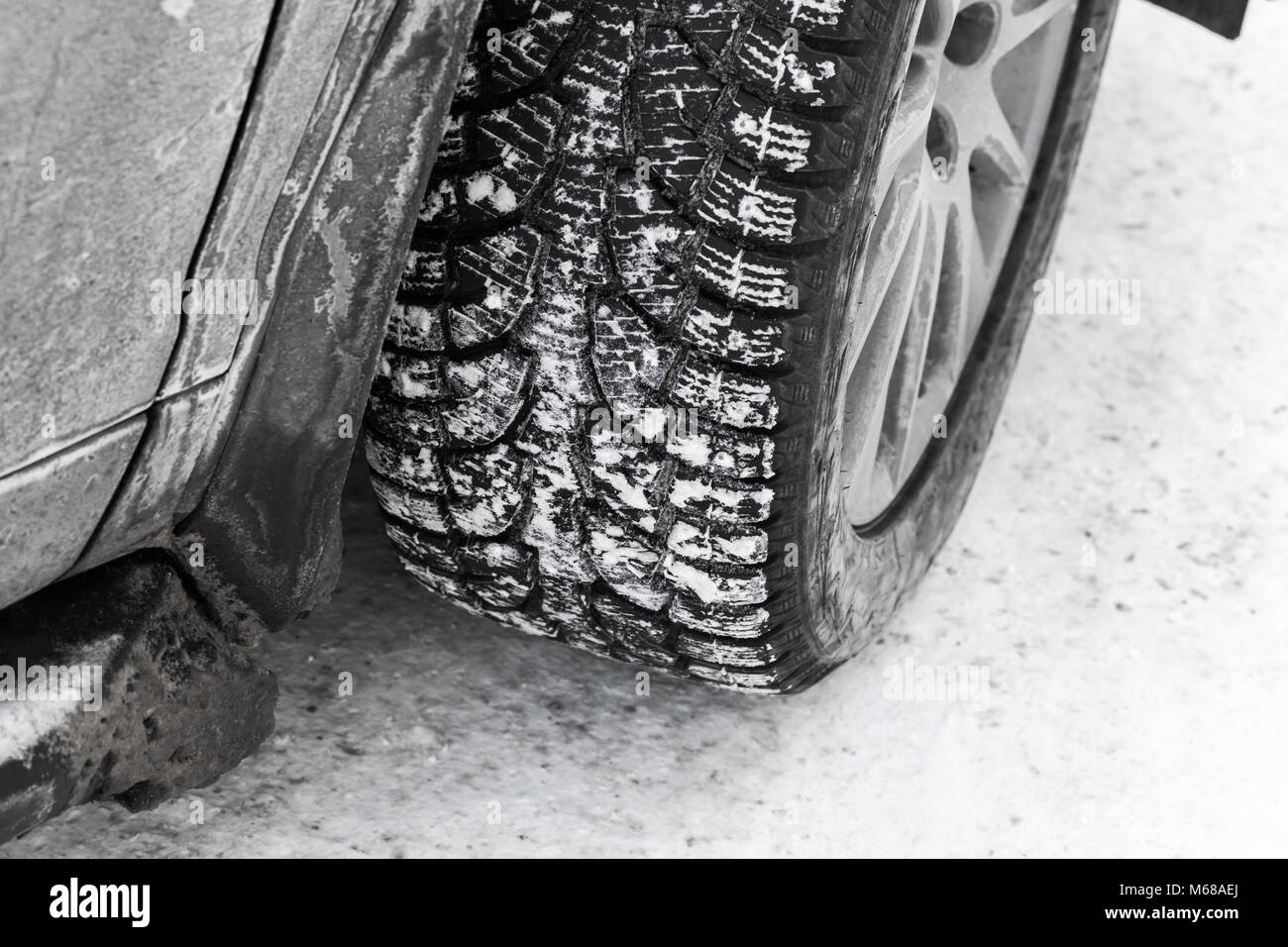 Car wheel on snow tire with metal studs, which improve traction on icy surfaces in winter season Stock Photo