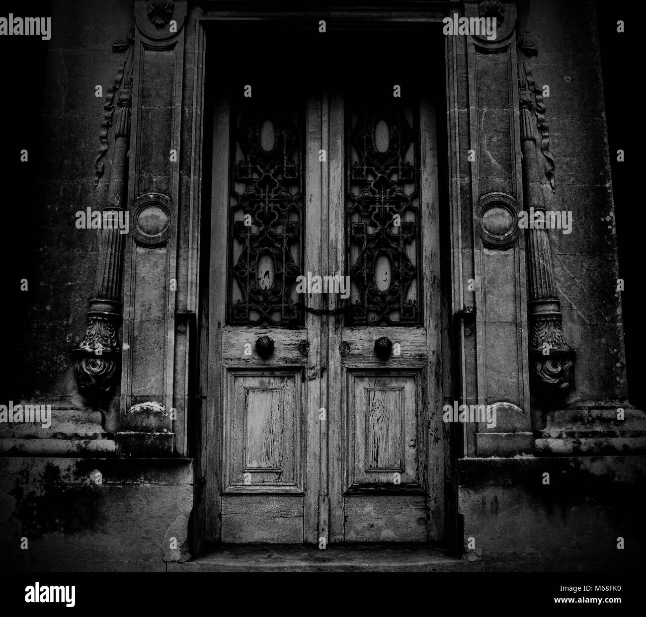 A Scary wooden Door of an Abandoned House with chains and rusted knobs in monochrome. Stock Photo