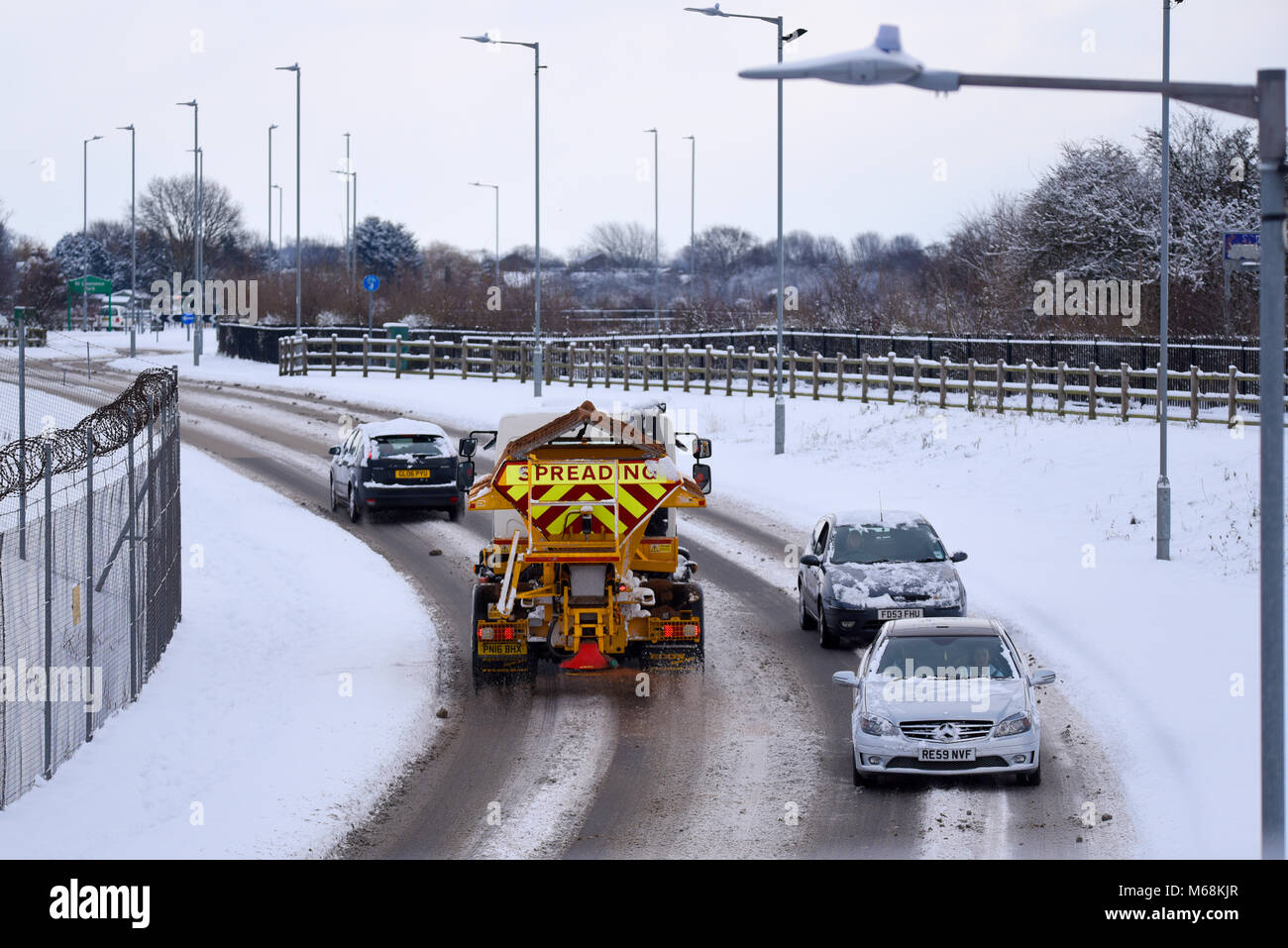 Grit salt spreading gritting on a snow covered road with cars during the beast from the east weather phenomenon. Space for copy Stock Photo