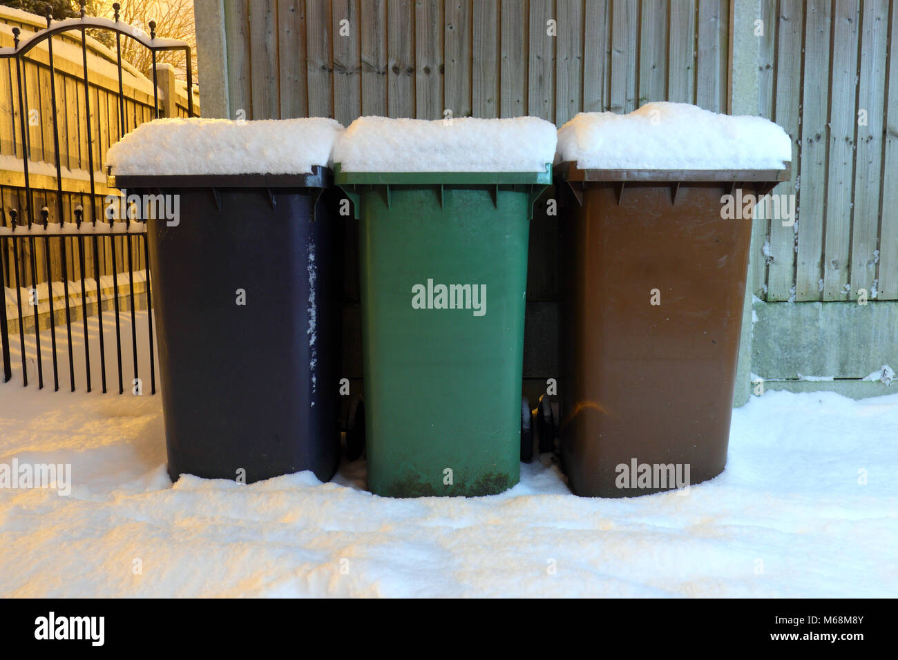 A set of wheelie bins with a thick layer of snow down a back alley in