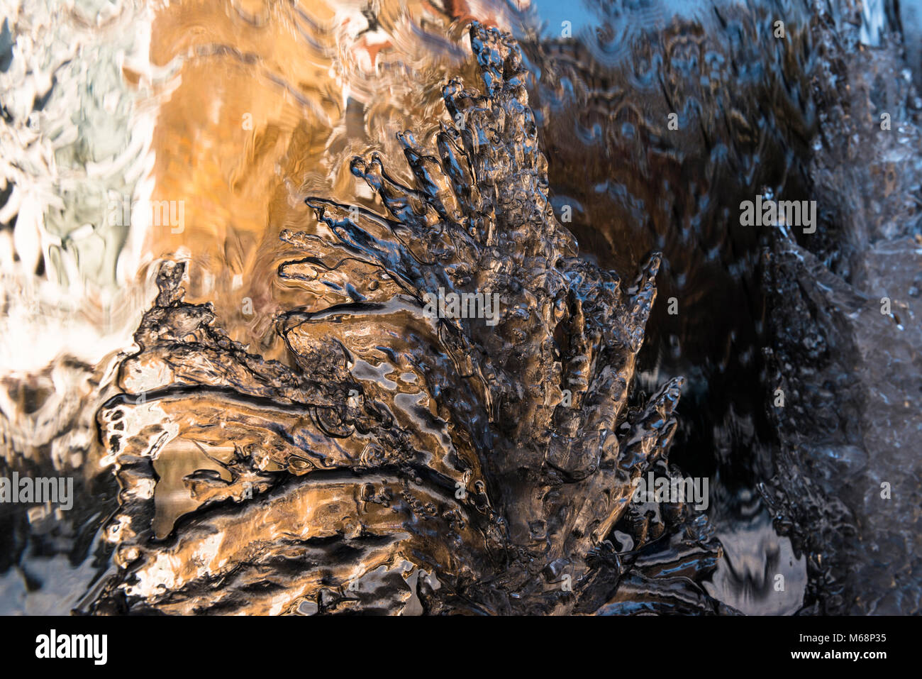 Impressionistic close up view of ice forming as a polished metal garden water feature freezes in winter with reflections of houses in sunlight. Stock Photo