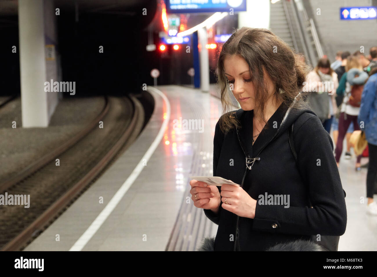 The girl passenger with a ticket in hand waiting for subway train. People in the background. Stock Photo