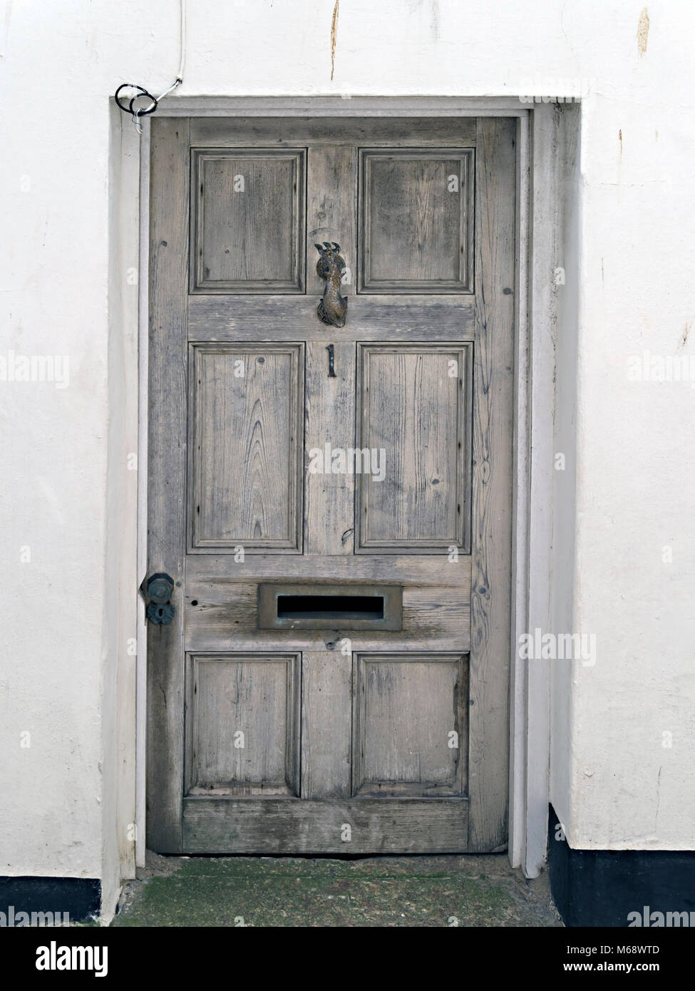Old distressed grey panelled wooden front door, with letter box, knocker and Number 1. Stock Photo