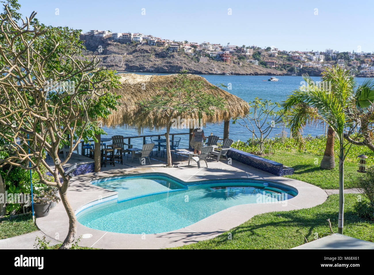 idyllic view Bahia San Carlos from guesthouse with jewel like pool & palapa providing shade for looking out at blue water & gated community across bay Stock Photo