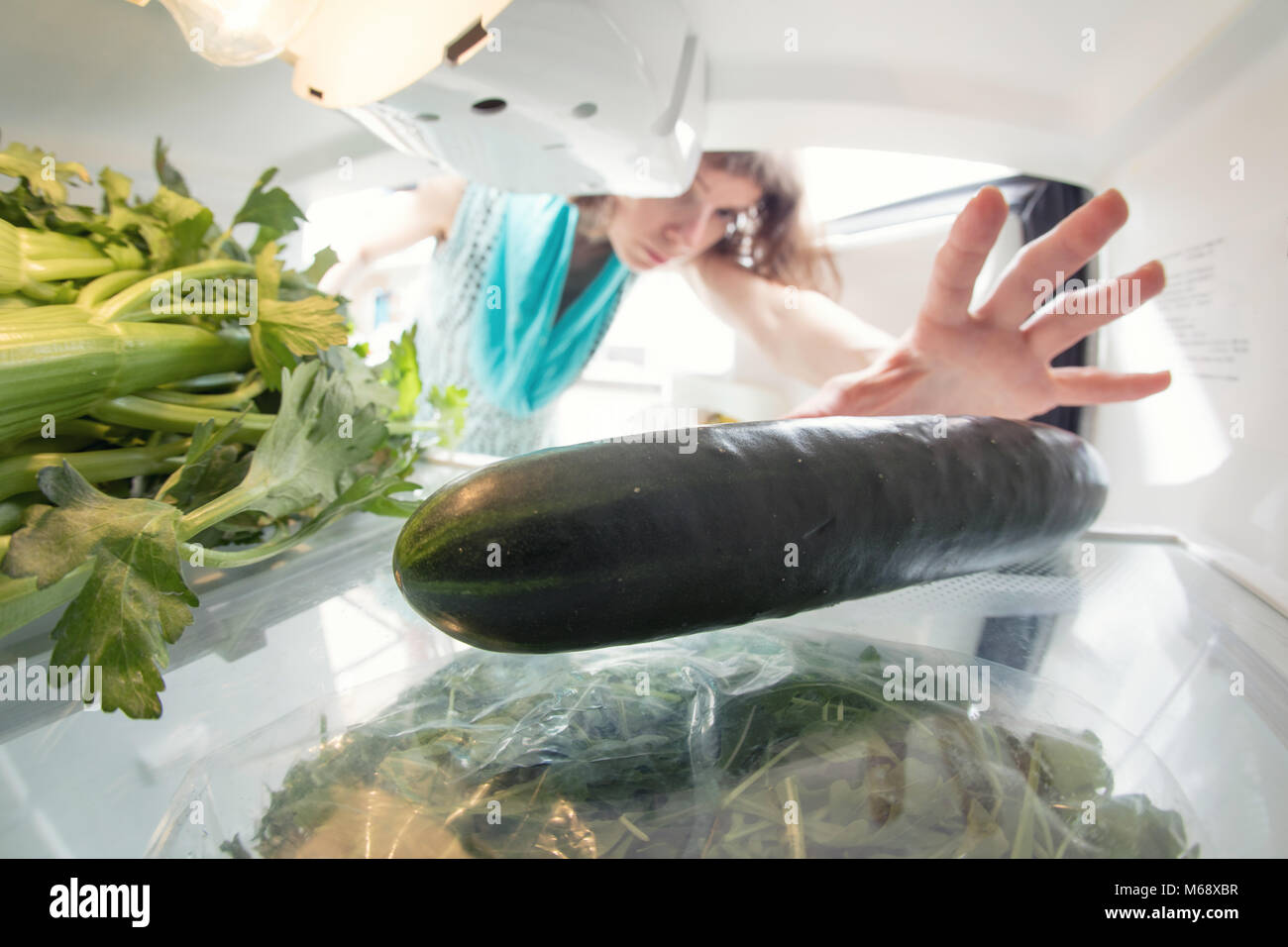 Healthy diet: A hand in an open refrigerator full of greens reaching for a cucumber. Stock Photo