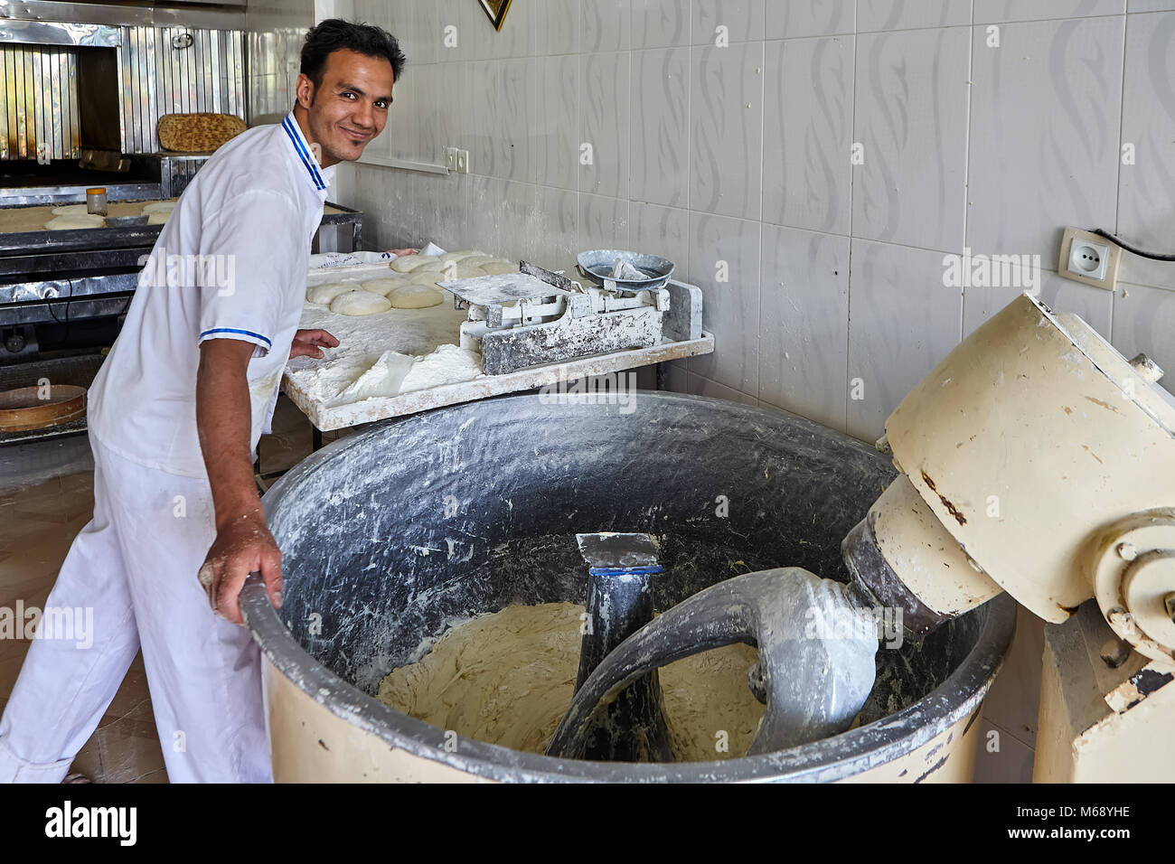 Kashan, Iran - April 27, 2017: A young Baker mixes a dough for an Iranian flat bread called barbari in his bakery using a kneading machine. Stock Photo