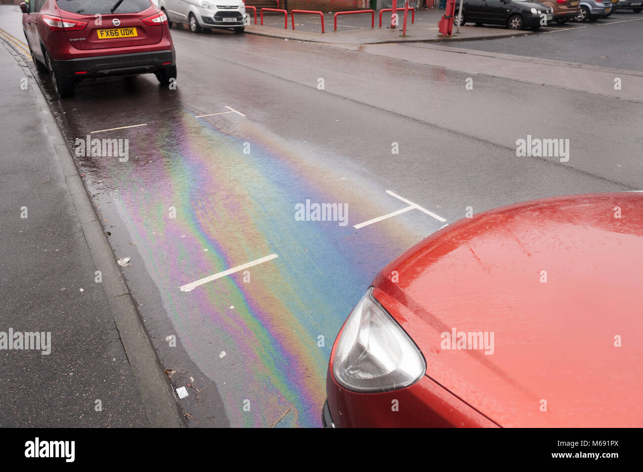 Light rainfall making the unseen petrol diesel oil spilling from cars clearly visible on road tarmac surface a pollutant flowing down covering surface Stock Photo