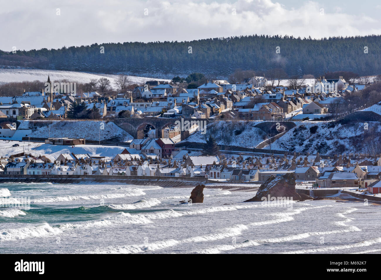 MORAY COAST SCOTLAND CULLEN BAY A STORMY SEA AND WINTER SNOW ON THE HOUSES IN THE TOWN Stock Photo