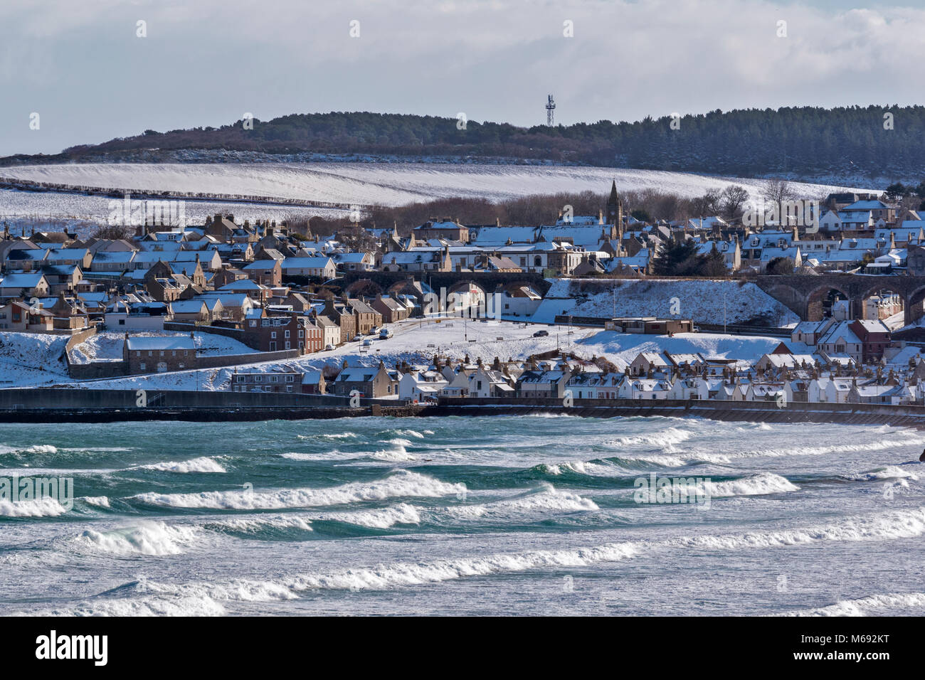 MORAY COAST SCOTLAND CULLEN BAY LARGE WAVES ON THE SEA AND WINTER SNOW ON THE HOUSES IN THE TOWN Stock Photo