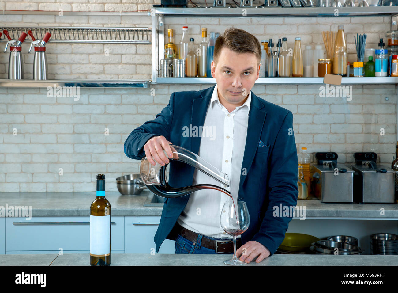Sommelier pouring red wine into glass from mixing bowl or decanter. Male waiter Stock Photo