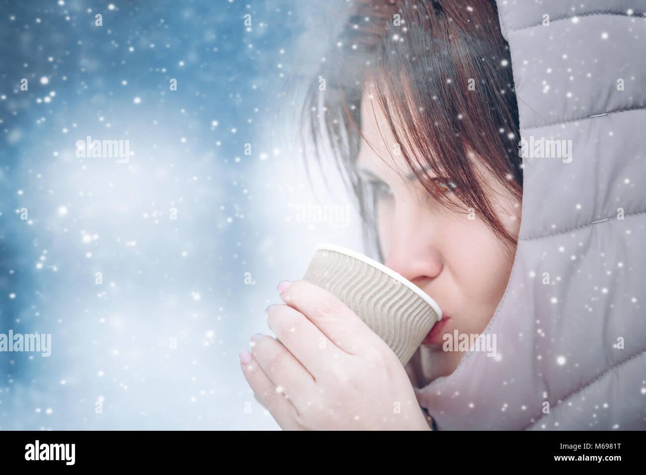 beautiful girl is drinking a hot drink from a cup in the winter in nature, tea, coffee. Snowy outdoor. Copy space Stock Photo