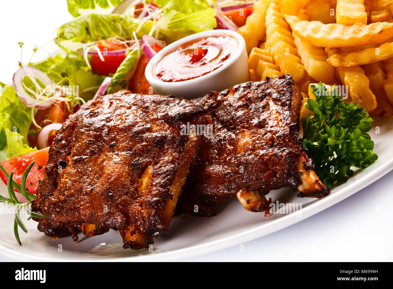 Grilled ribs, French fries and vegetables on white background Stock