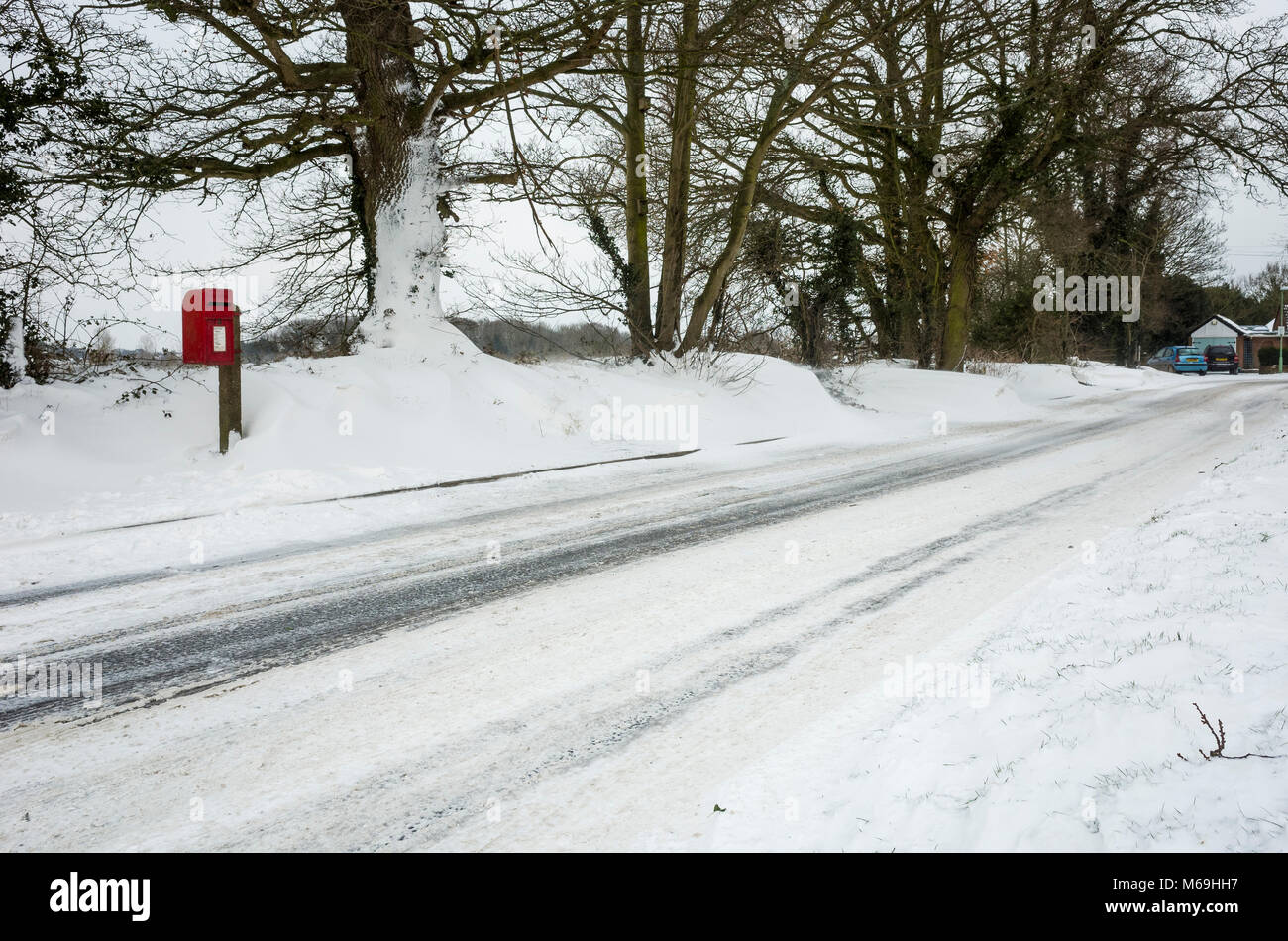 Ipswich, England. 1st March 2018.  A secluded Royal Mail postbox on side of a snow laden road following 'The Beast From The East' storm.  Snow drifts have completely blocked the path up to the road side, with snow built-up in excess of 30cm high.  Tire tracks from passing traffic can be seen along the road.  Photographed with a Ricoh GRII camera. Stock Photo
