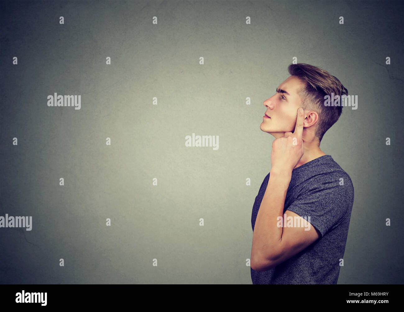 Side view of casual young man thinking on problem looking away in concentration on gray. Stock Photo