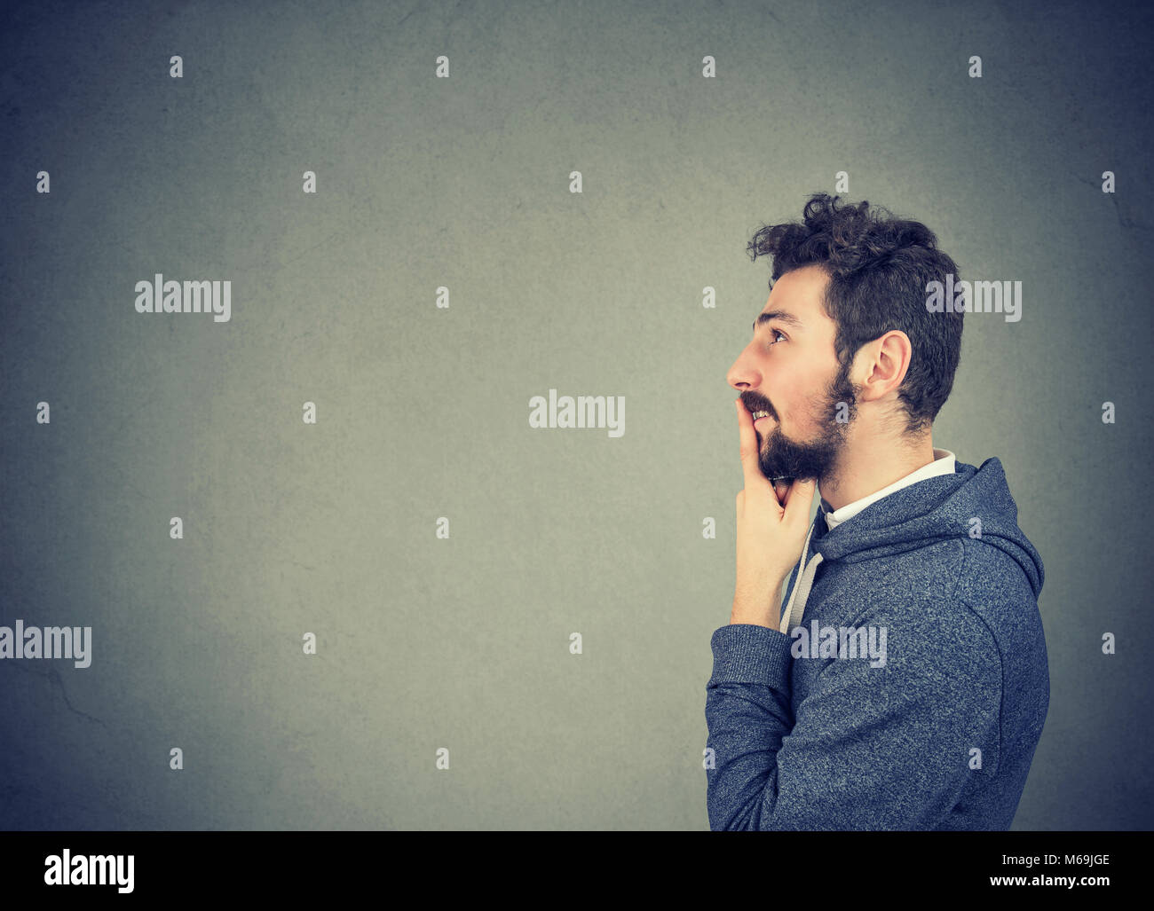 Side view of casual happy young man thinking on problem looking away in concentration on gray. Stock Photo