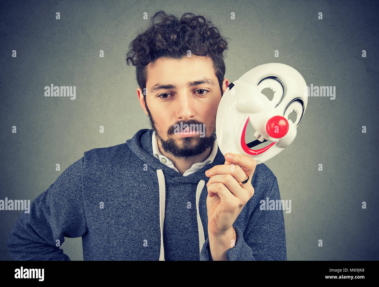 Young bearded upset man covering personality with happy clown mask on