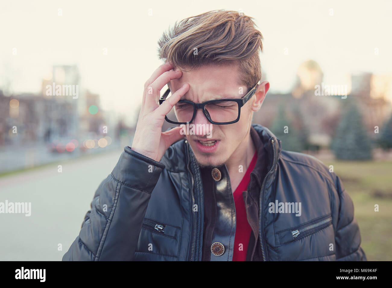 Young casual man frowning from headaches and noise while standing on urban background. Stock Photo