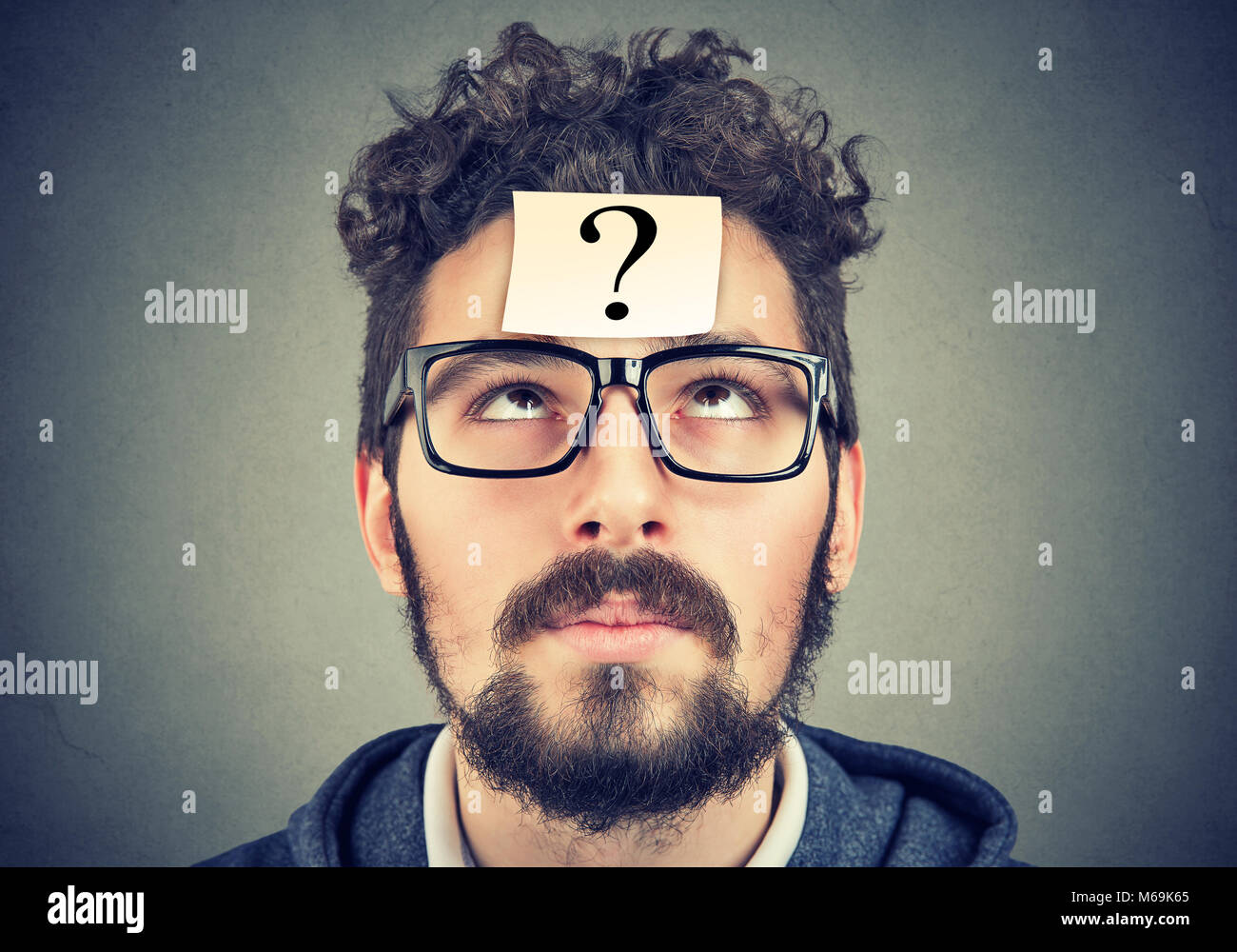 thinking man with question mark looking up on gray wall background Stock Photo