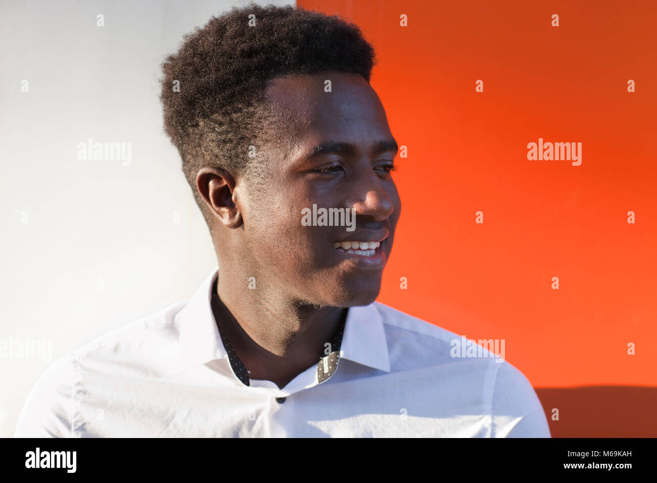 Handsome young black man looking to the side and smiling in front of orange and white divided background Stock Photo