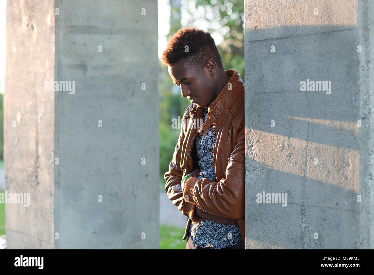 Handsome thoughtful young black man leaning on a wall looking down Stock Photo