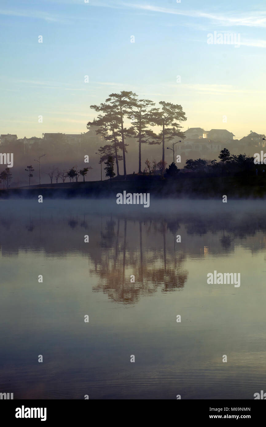 Beautiful landscapes of Da Lat city at morning with lake in fog, pine tree reflect on water, scenery in purple, this place is romantic destination for Stock Photo