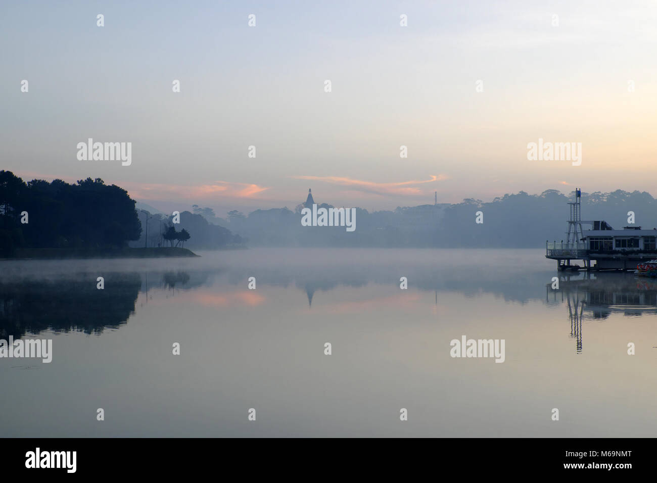 Wonderful scenery of Da Lat city at sunrise, Thuy Ta restaurant reflect on water, yellow sky and lake in fog make romantic place for Vietnam travel Stock Photo