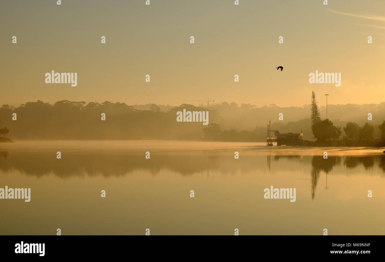 Wonderful scenery of Da Lat city at sunrise, Thuy Ta restaurant reflect on water, yellow sky and lake in fog make romantic place for Vietnam travel Stock Photo