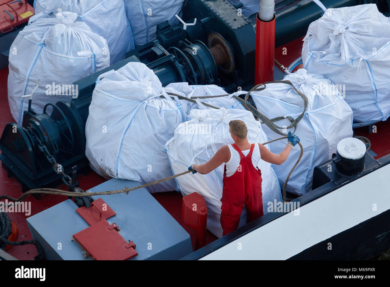 Worker in a red suit on a cargo ship. Stock Photo