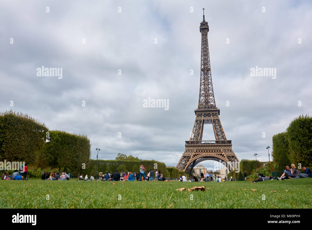 View of the Eiffel Tower from the field in the fall in cloudy weather amidst a resting people. Stock Photo