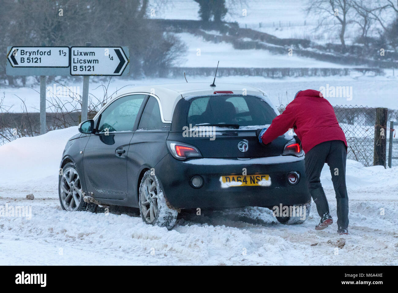 Lixwm, Flintshire, Wales, UK 2nd March 2018, UK Weather:  Storm Emma bringing stormy blizzard conditions in the uplands Flintshire with Met Office Warnings in place. Many rural areas cut off with snow ploughs and tractors attempting to clear main roads only with more snow forecasted from midday. A passer by assisting a driver to gain traction on a rural road in the vilage of Lixwm, Flintshire, Wales  © DGDImages/Alamy Live News Stock Photo
