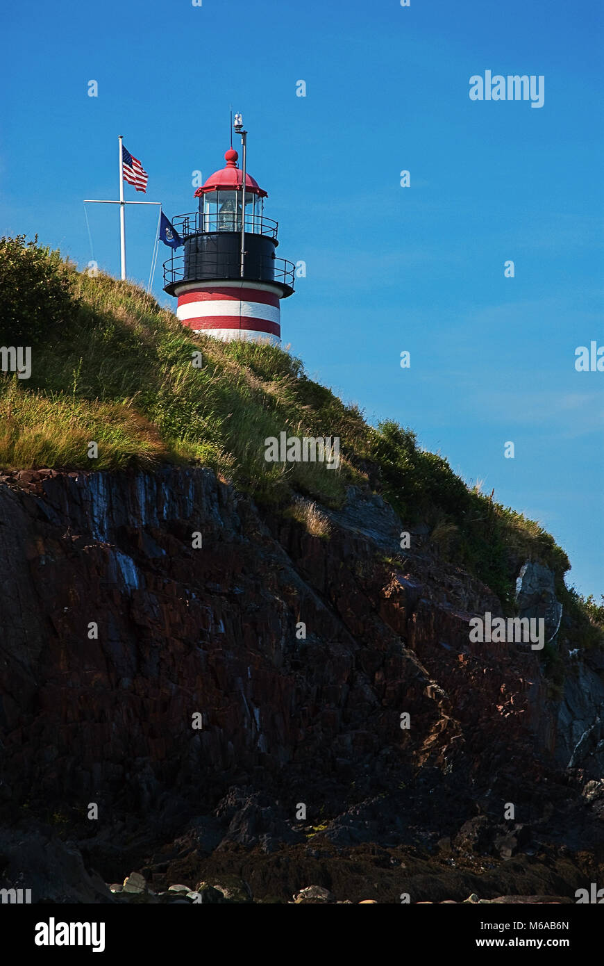 West Quoddy Head Lighthouse, painted in red and white stripes like a candy cane, overlooks a rocky cliff. The beacon resides in Lubec, Maine. Stock Photo