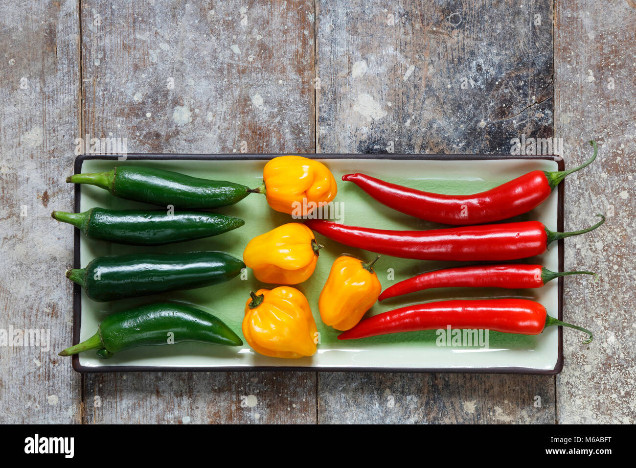 Close up of red, green and yellow hot peppers arranged on rectangular tray on old  wooden table Stock Photo