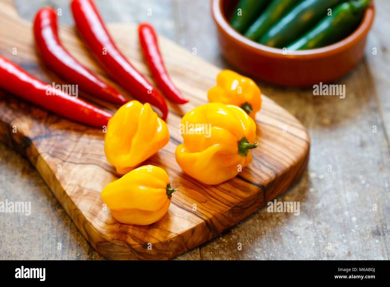 Red and yellow hot peppers on cutting board with green peppers in a bowl Stock Photo