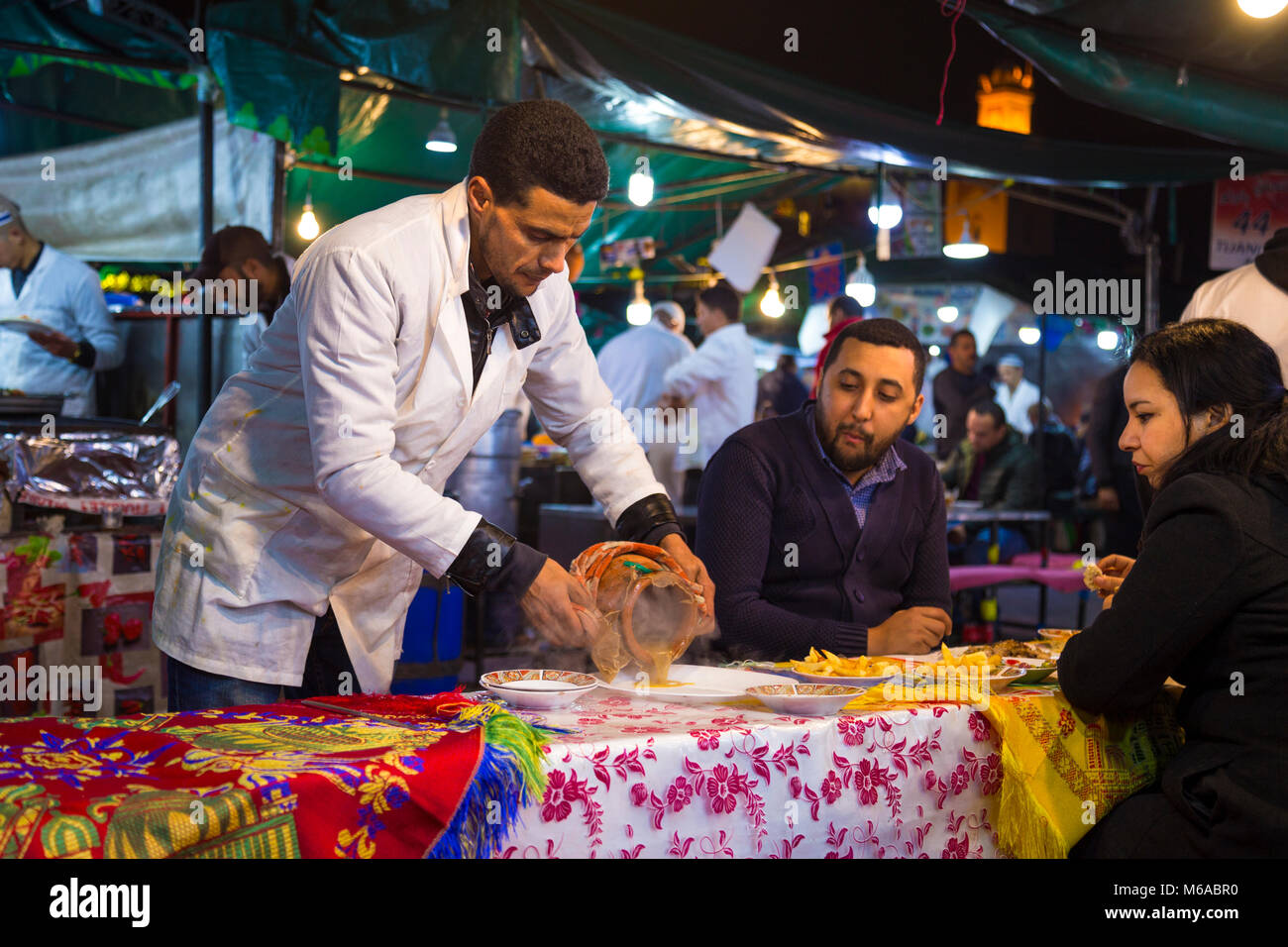 Waiter poring out a tangia from a ceramic pot onto a plate at the food market in Jemaa el-Fnaa, Marrakech, Morocco Stock Photo