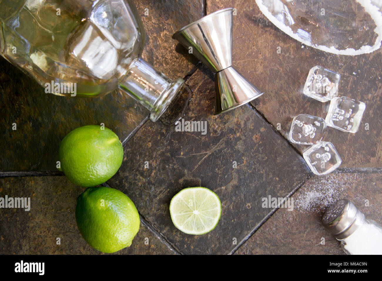Ingredients for margarita cocktail with alcohol bottle, limes, salt and