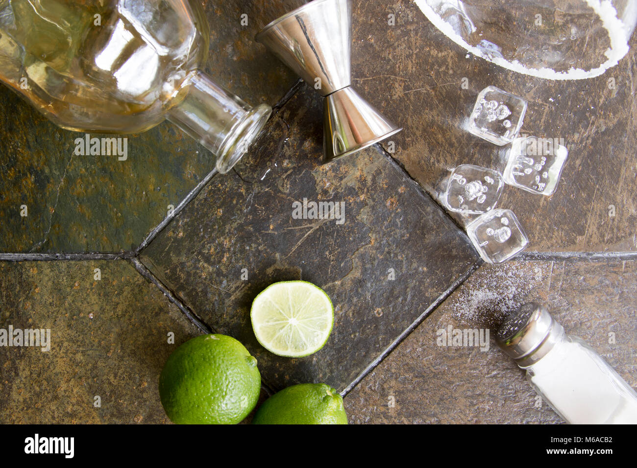 Ingredients for margarita cocktail with alcohol bottle, limes, salt and