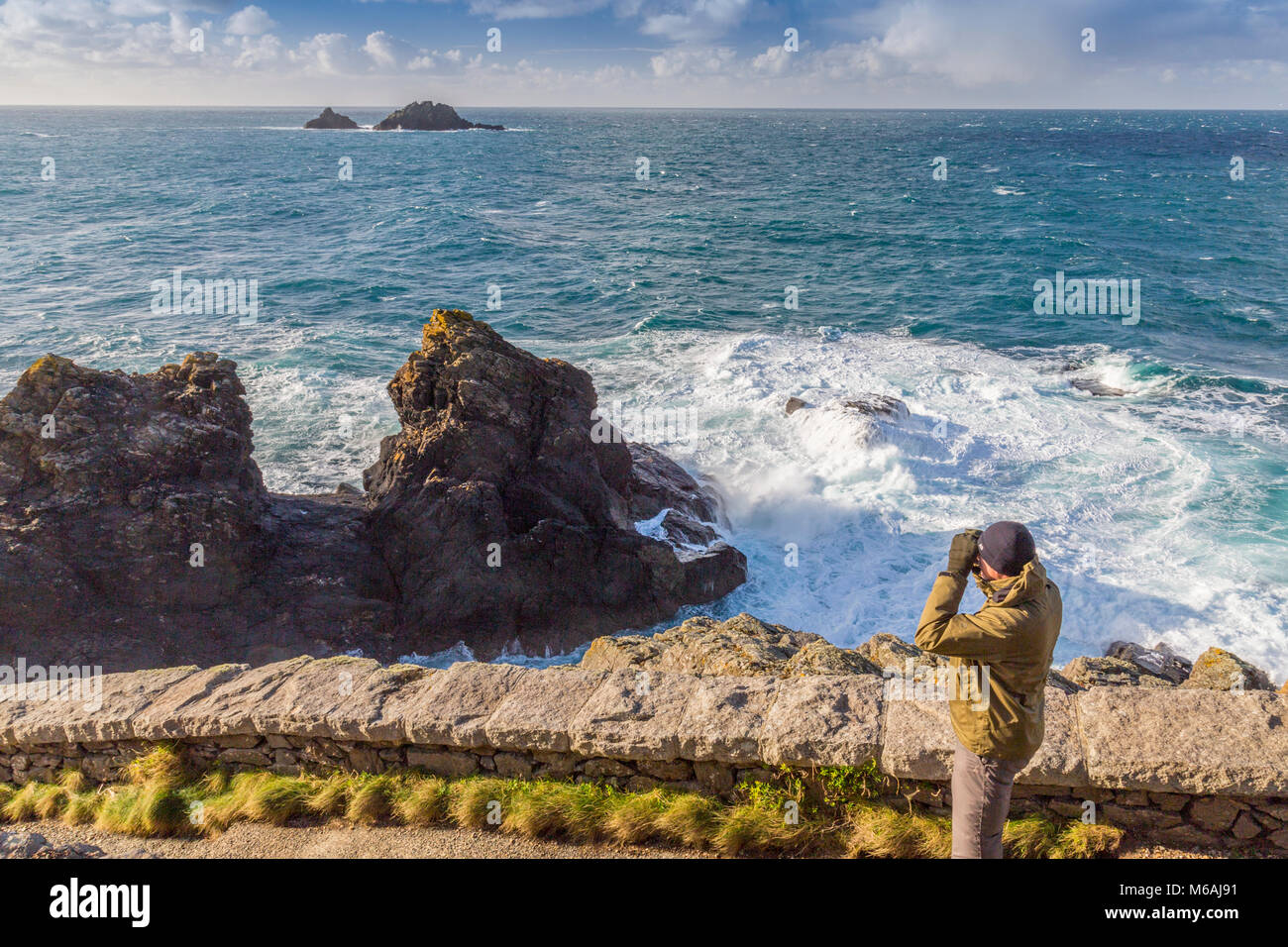 A birdwatcher on the South West Coast Path at Cape Cornwall with the Brisons rocks beyond, England, UK Stock Photo