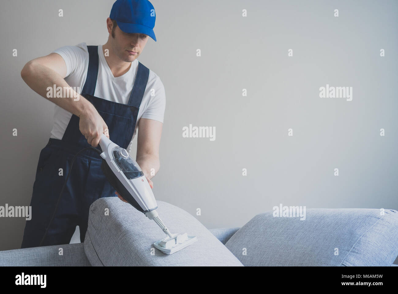Man in uniform cleaning sofa with dry steam cleaner. Place for text