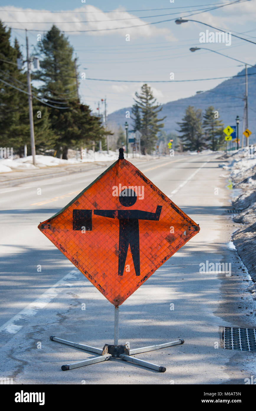 A torn, worn and dirty sign on a street indicating a flagman and construction is ahead on the empty road in Speculator, NY USA Stock Photo