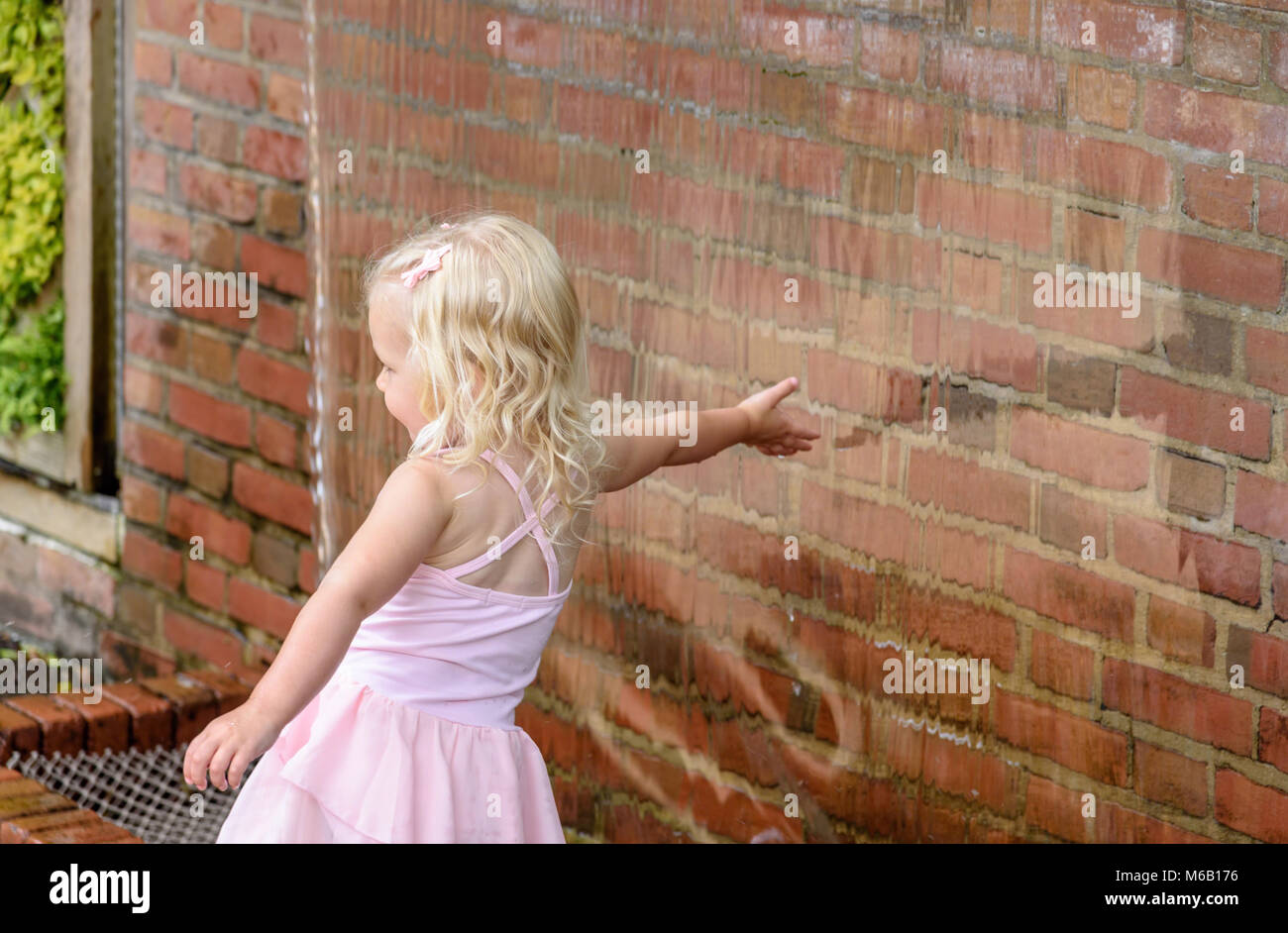 little girl reaching toward waterfall with hand outdoors in summer Stock Photo