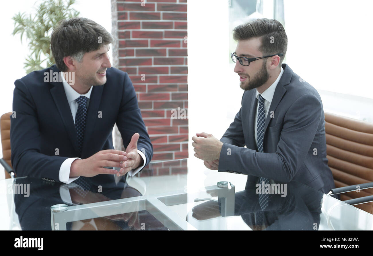 Two businessmen discussing tasks sitting at office table. Stock Photo