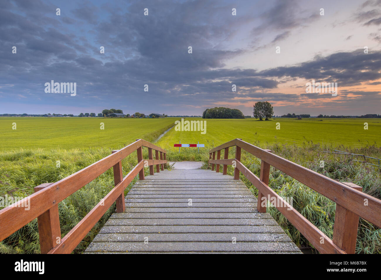 Wooden bridge in agricultural landscape against beautiful colored sunset Stock Photo