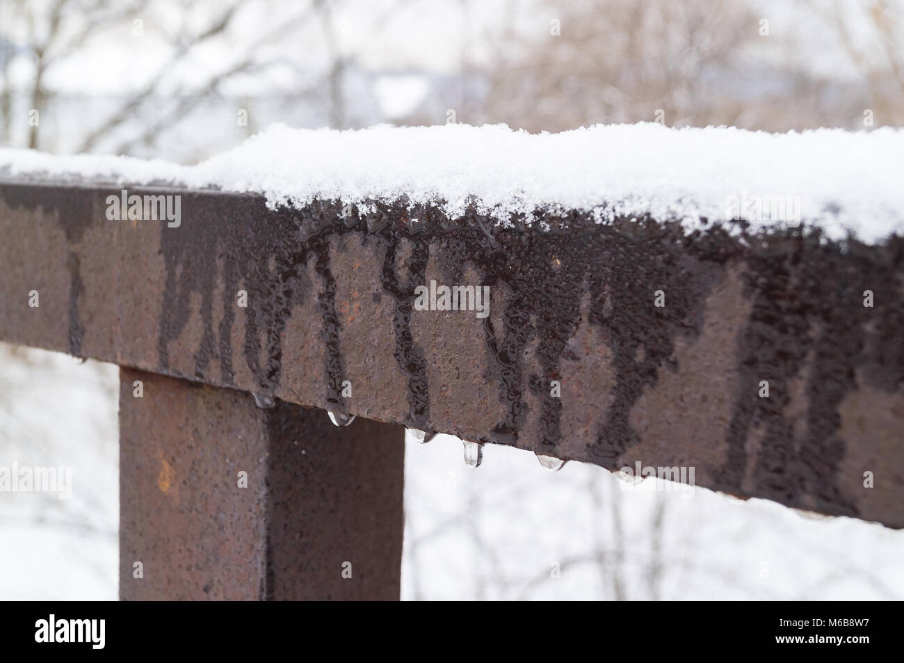 The snow melts on metal rails during the thaw of the first day of spring. Greetings of Spring Stock Photo