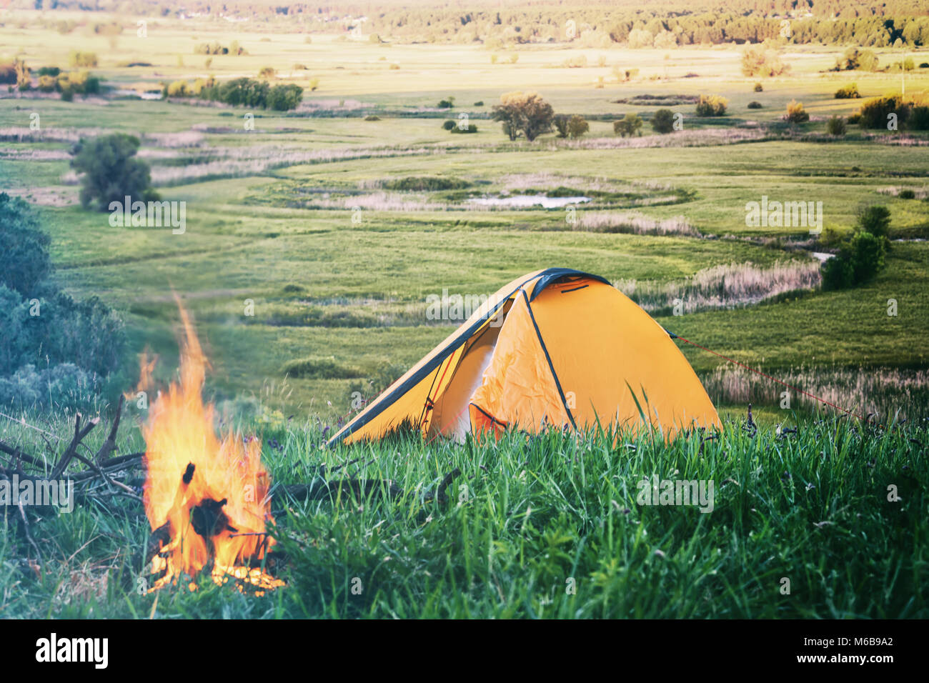 Orange tent with fire in field with green grass Stock Photo